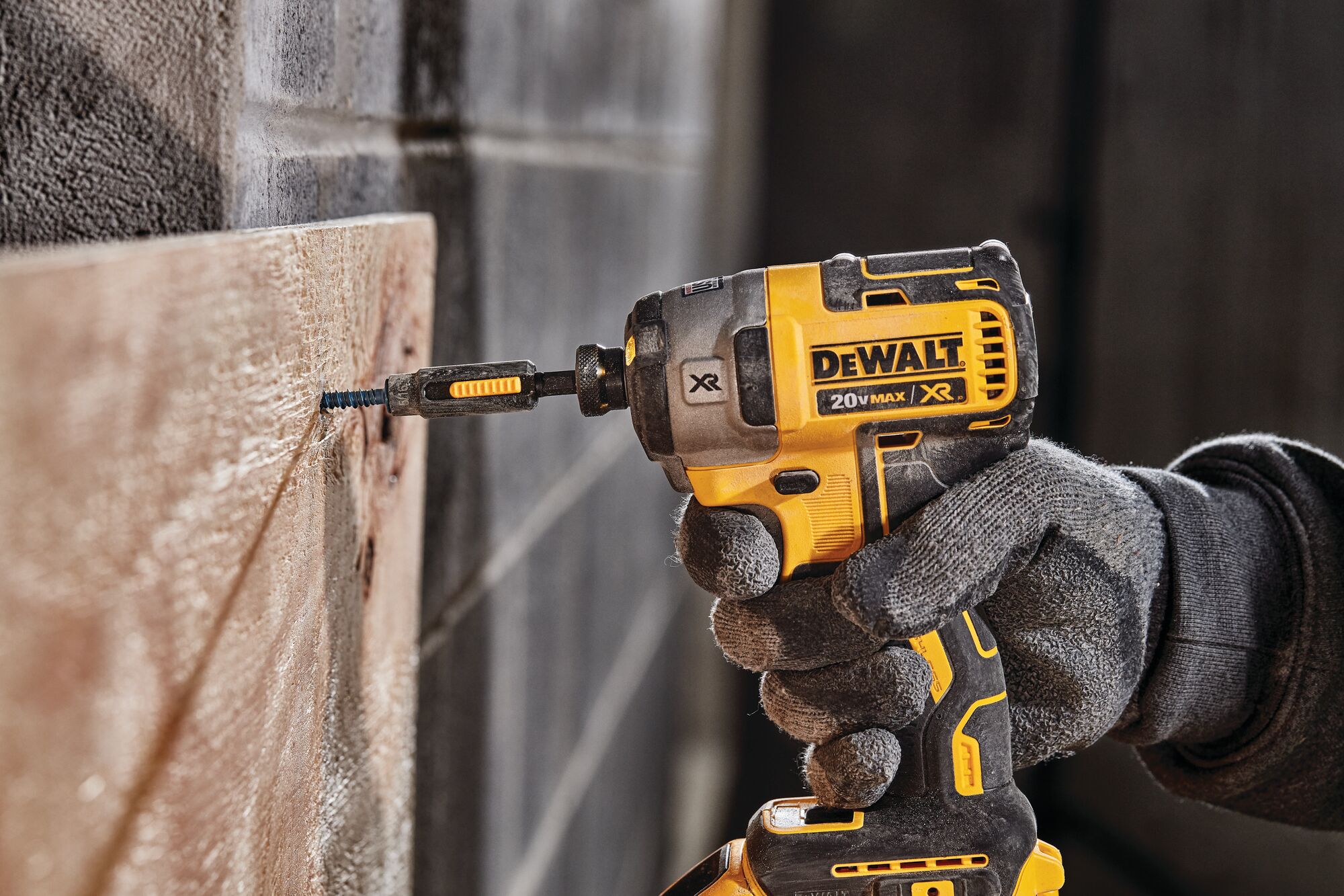 A person wearing work gloves uses a yellow and black DEWALT 20V MAX XR cordless impact driver to drive a screw into a wooden board. (dewalt.ca)