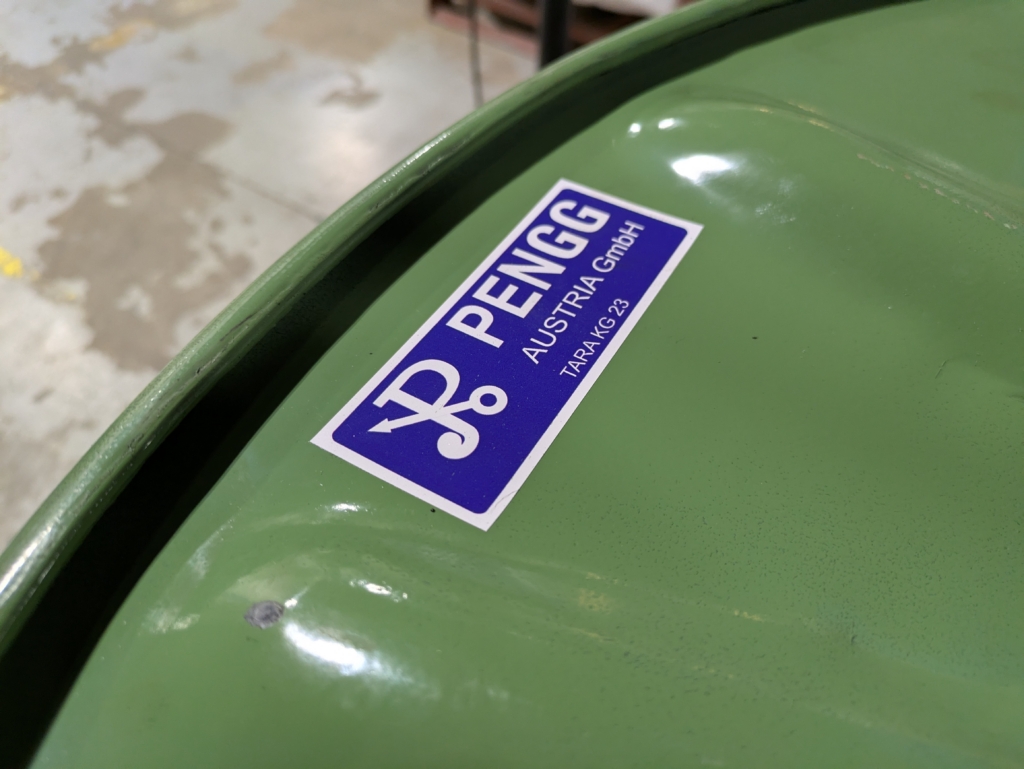 The top of an empty spool of wire. The spool is green and the sticker reads PENGG Austria GmbH TARA KG 23