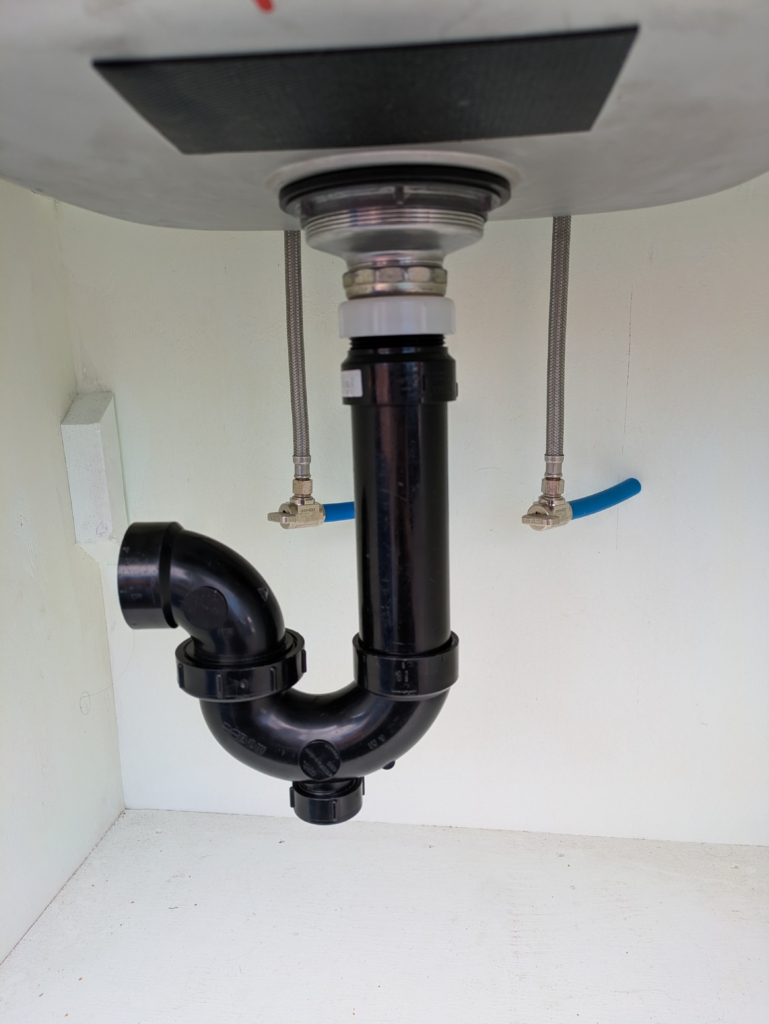 Kitchen drain with black drain pipe and P-trap. The P-trap has a cleanout.