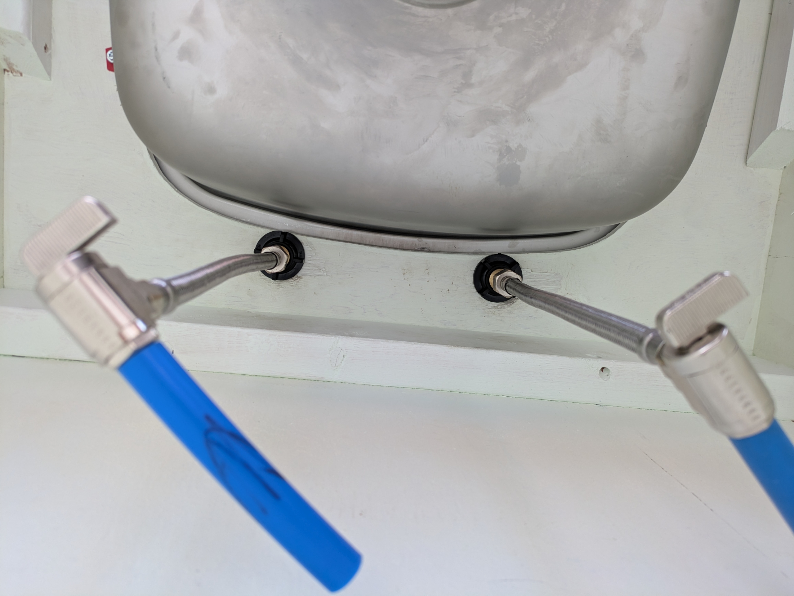 The underside of a sink with faucet supply lines installed